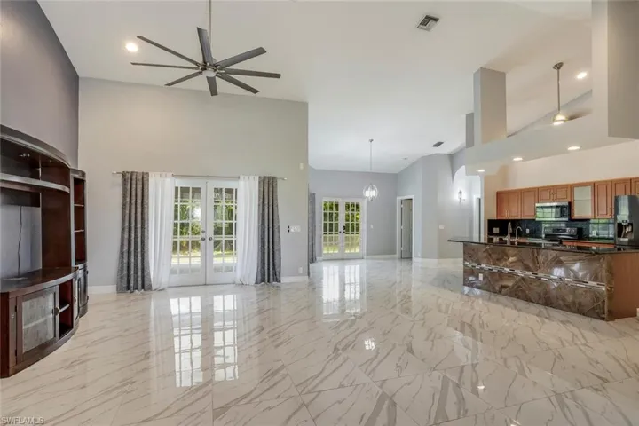 Living room with french doors, high vaulted ceiling, ceiling fan with notable chandelier, and sink