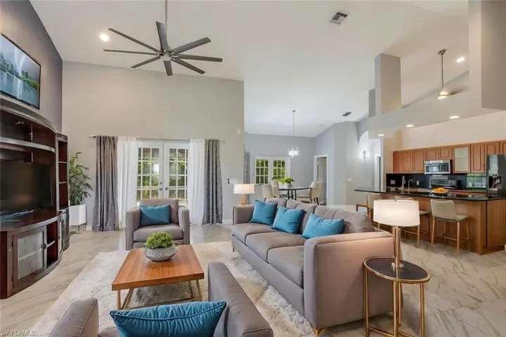 Living room featuring ceiling fan with notable chandelier, sink, and high vaulted ceiling