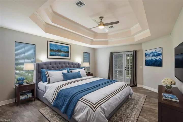 Bedroom featuring a raised ceiling, ceiling fan, dark hardwood / wood-style flooring, and crown molding