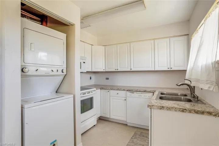 Kitchen featuring white appliances, white cabinets, sink, stacked washer and dryer, and light tile patterned flooring