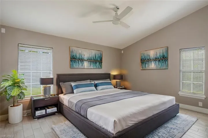 Bedroom with ceiling fan, vaulted ceiling, light hardwood / wood-style floors, and multiple windows