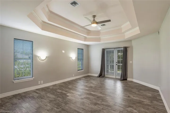 Unfurnished room with a raised ceiling, crown molding, ceiling fan, and dark wood-type flooring