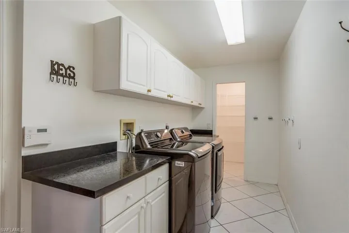 Clothes washing area featuring washing machine and dryer, light tile patterned floors, and cabinets