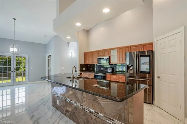 Kitchen featuring dark stone counters, a kitchen island with sink, hanging light fixtures, and appliances with stainless steel finishes
