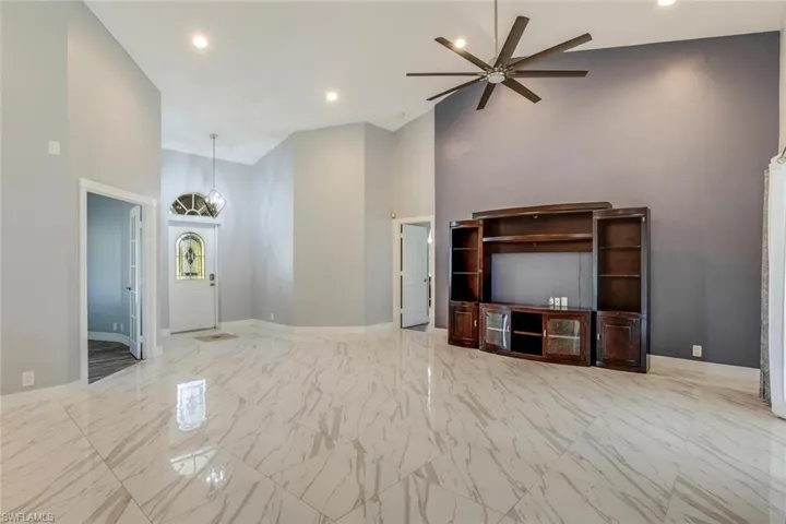 Unfurnished living room featuring ceiling fan with notable chandelier and high vaulted ceiling
