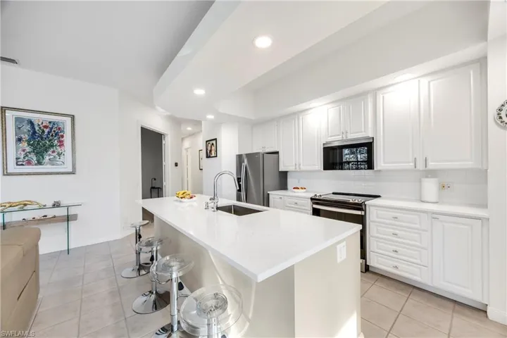 Kitchen with a kitchen bar, stainless steel appliances, white cabinets, light tile patterned floors, and light stone countertops