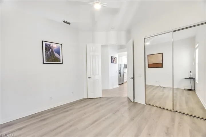 Unfurnished bedroom with light wood-style floors, a ceiling fan, stainless steel refrigerator with ice dispenser, and a closet