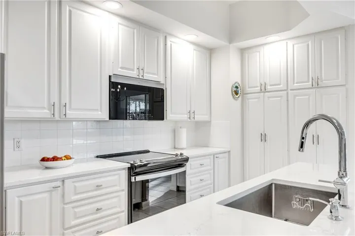 Kitchen with electric stove, white cabinets, black microwave, and tasteful backsplash