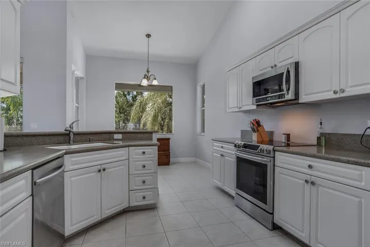 Kitchen with dark countertops, hanging light fixtures, appliances with stainless steel finishes, white cabinetry, and a sink