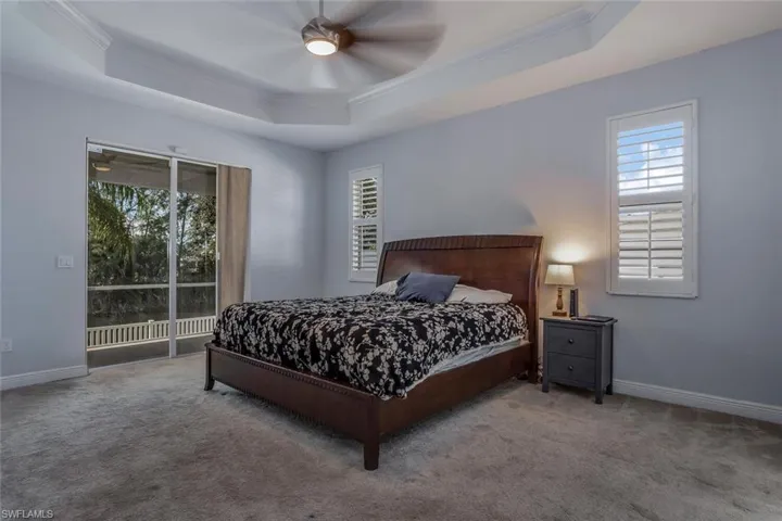 Carpeted bedroom featuring crown molding, a raised ceiling, a ceiling fan, access to outside, and baseboards