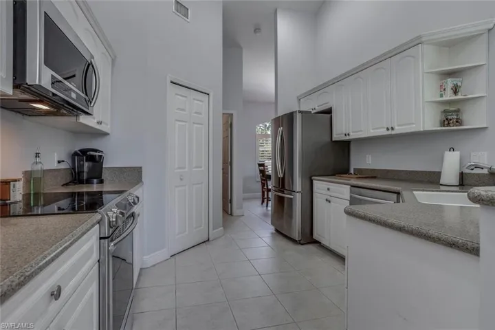 Kitchen with light tile patterned floors, stainless steel appliances, a sink and white cabinetry