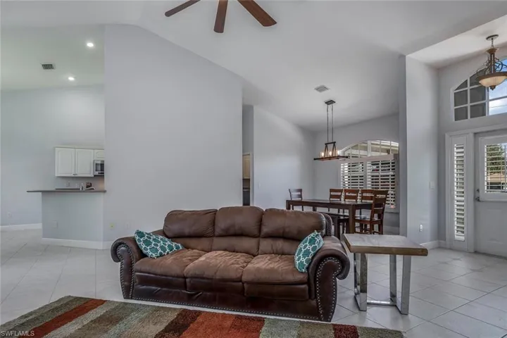 Living room with ceiling fan with notable chandelier, light tile patterned flooring and baseboards