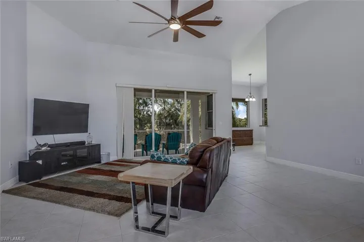 Living area featuring light tile patterned floors, high vaulted ceiling, ceiling fan with notable chandelier, and baseboards
