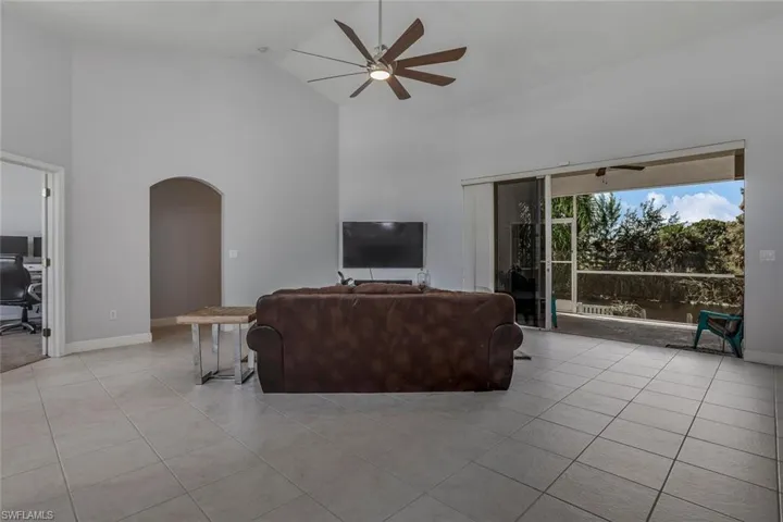 Living area featuring arched walkways, high vaulted ceiling, light tile patterned floors, and a ceiling fan