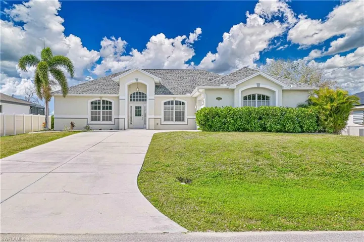 View of front facade with concrete driveway, fence, a front lawn, and stucco siding