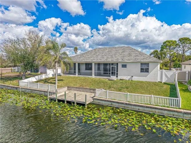Back of house featuring a water view, a sunroom, a fenced backyard, and a yard