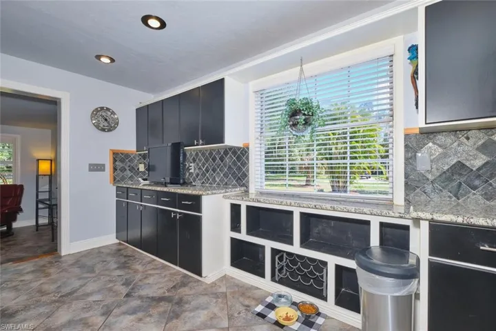 Kitchen with decorative backsplash, dark cabinetry, light stone countertops, and baseboards