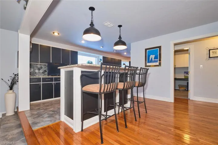 Kitchen featuring dark cabinetry, light wood-style floors, pendant lighting, decorative backsplash, and a kitchen breakfast bar