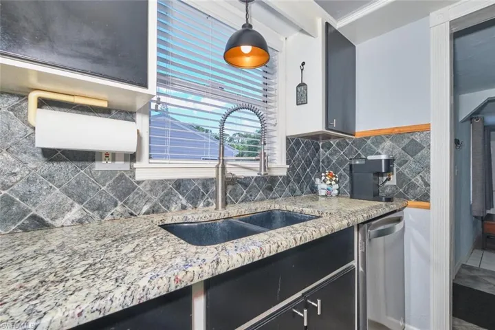 Kitchen featuring stainless steel dishwasher, a sink, backsplash, and light stone counters