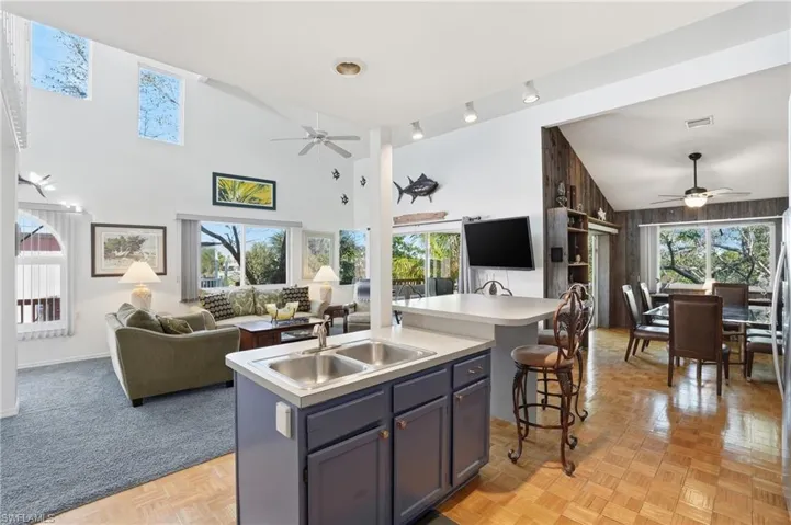 Kitchen featuring ceiling fan, open floor plan, a kitchen island with sink, high vaulted ceiling, and wooden walls - Virtually Edited Image