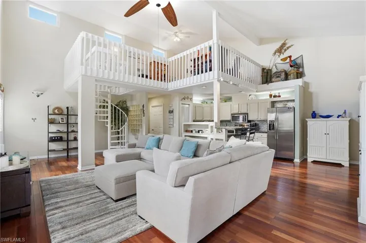 Living area featuring stairs, dark wood finished floors, a ceiling fan, beamed ceiling, and high vaulted ceiling - Virtually Edited Image