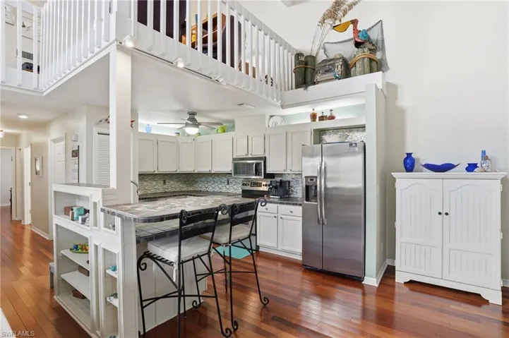Kitchen with stainless steel appliances, a high ceiling, a breakfast bar, white cabinetry, and dark wood-style flooring