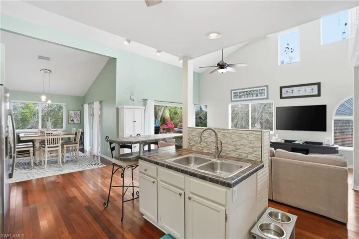 Kitchen with open floor plan, a breakfast bar, high vaulted ceiling, white cabinetry, and dark wood-type flooring - Virtually Edited Image