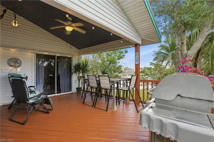 Wooden deck featuring a grill, outdoor dining area, and a ceiling fan - Virtually Edited Image
