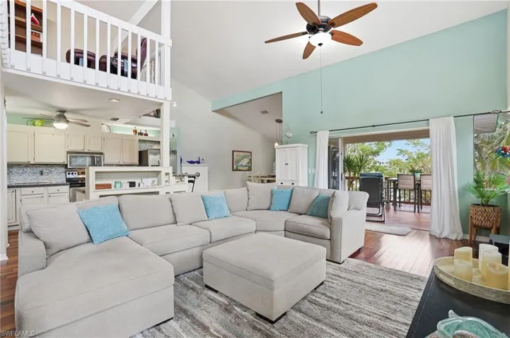 Living room featuring a ceiling fan, high vaulted ceiling, and hardwood / wood-style flooring - Virtually Edited Image