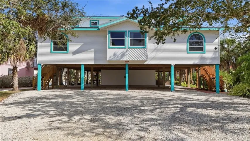 Coastal inspired home featuring a carport, stairs, and gravel driveway - Virtually Edited Image
