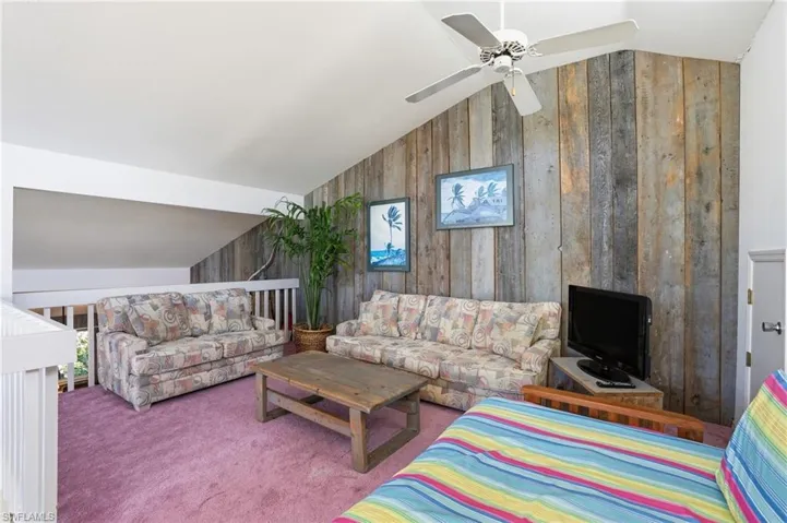 Living area featuring wooden walls, lofted ceiling, carpet floors, ceiling fan, and an accent wall - Virtually Edited Image