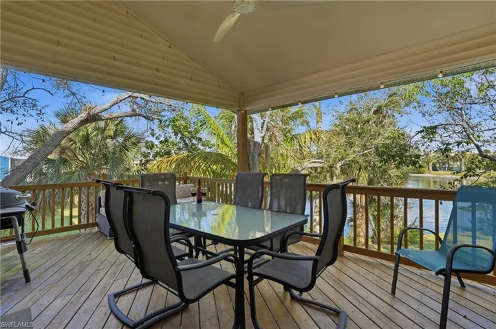 Wooden deck featuring a water view, outdoor dining space, a grill, and ceiling fan - Virtually Edited Image