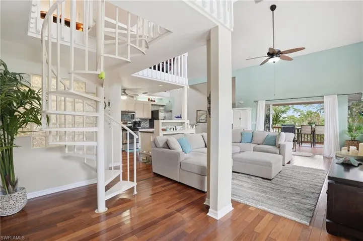 Living area featuring ceiling fan, a high ceiling, dark wood-style floors, and stairs - Virtually Edited Image