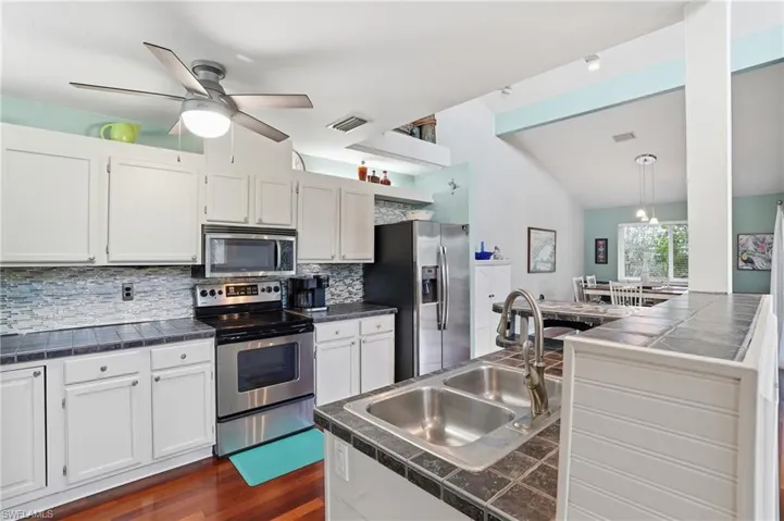 Kitchen featuring appliances with stainless steel finishes, white cabinets, decorative backsplash, and tile counters - Virtually Edited Image