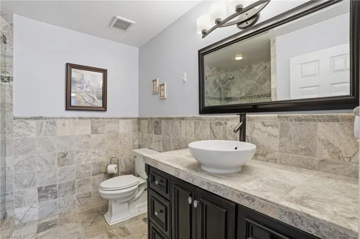 Full bathroom featuring vanity, tile walls, wainscoting, and tiled shower - Virtually Edited Image