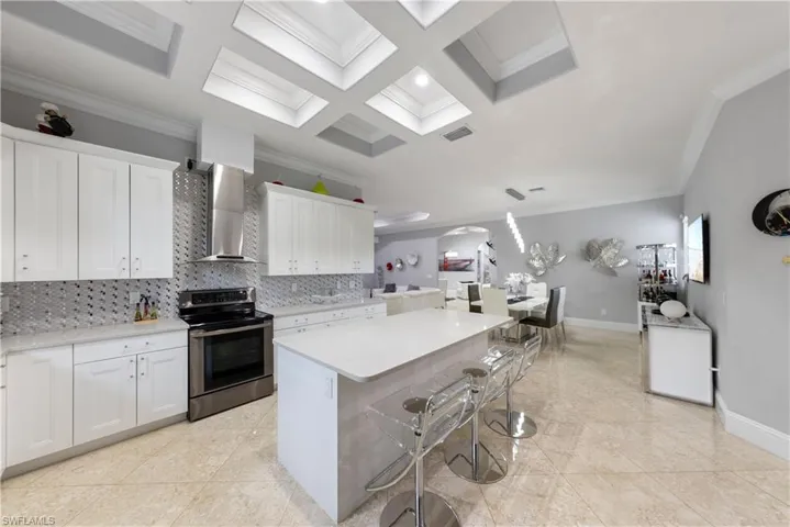 Kitchen featuring wall chimney exhaust hood, ornamental molding, electric range, and white cabinets