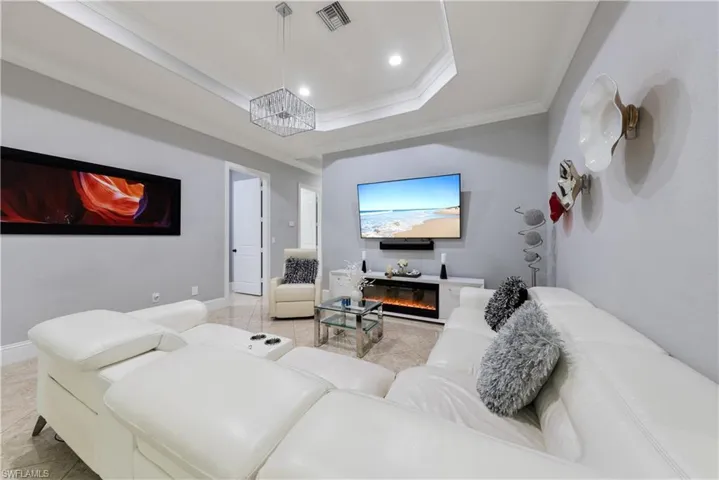 Living room with an inviting chandelier, a tray ceiling, crown molding, and light tile patterned floors