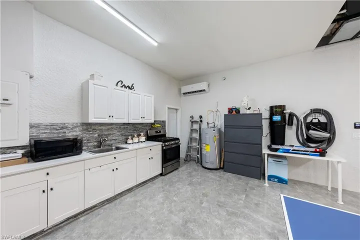 Kitchen featuring electric water heater, sink, an AC wall unit, white cabinets, and stainless steel gas range oven