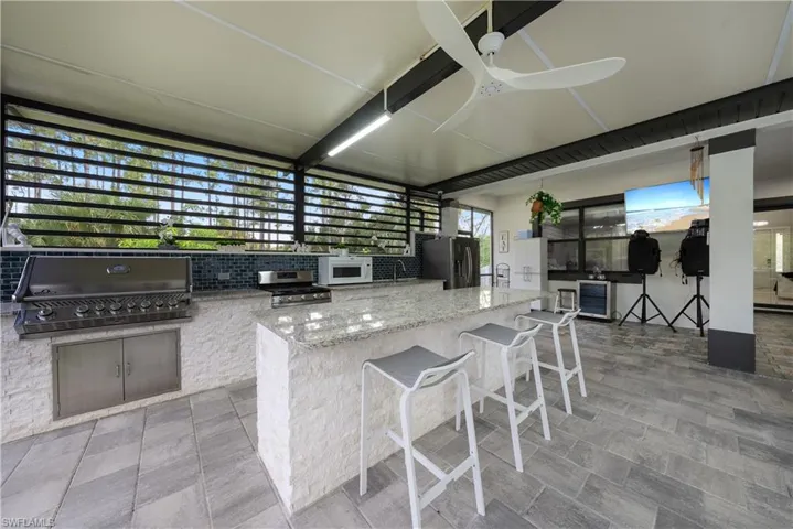 Kitchen featuring light stone counters, ceiling fan, stainless steel appliances, a kitchen breakfast bar, and decorative backsplash