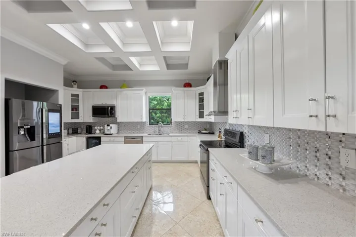 Kitchen featuring light stone counters, stainless steel appliances, crown molding, and white cabinetry