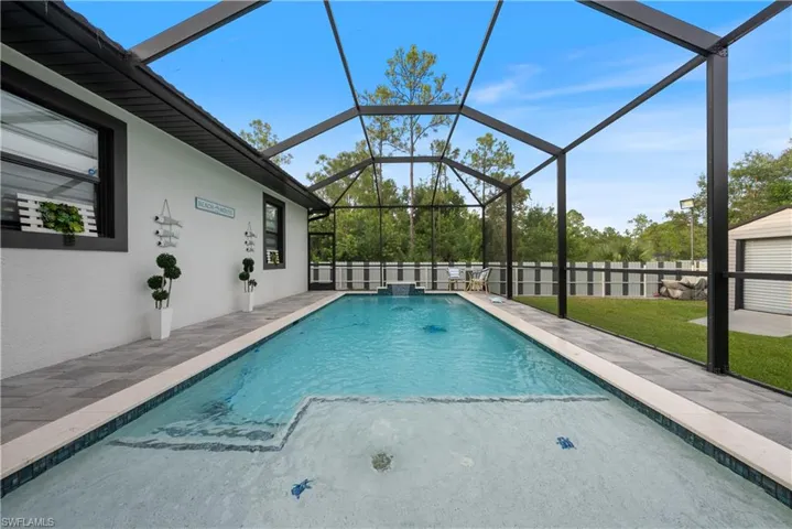 View of swimming pool with glass enclosure, a patio, and pool water feature