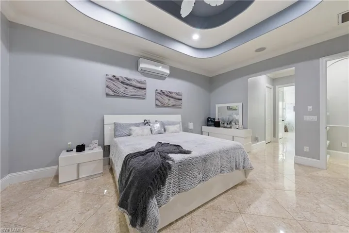 Bedroom featuring crown molding, a tray ceiling, ceiling fan, ensuite bathroom, and a wall unit AC