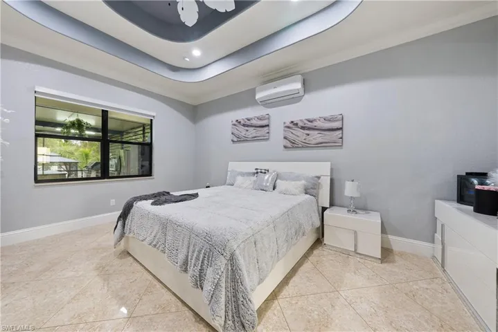 Bedroom with ornamental molding, ceiling fan, a raised ceiling, and a wall mounted AC