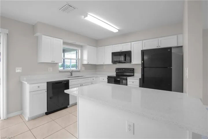Modern kitchen featuring white cabinetry, light countertops, black appliances, a central island, and tiled flooring