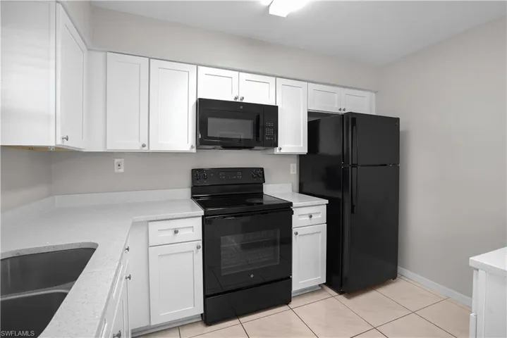 Contemporary kitchen featuring white cabinetry, light-toned countertops, and black appliances including an oven range with microwave and a refrigerator