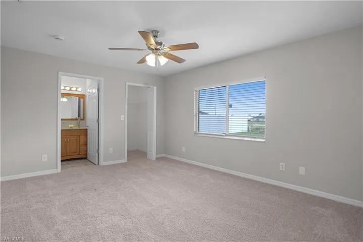 Carpeted room featuring a ceiling fan with light fixture, a window with horizontal blinds, a doorway to a bathroom with a wood-finish vanity, and a separate closet doorway
