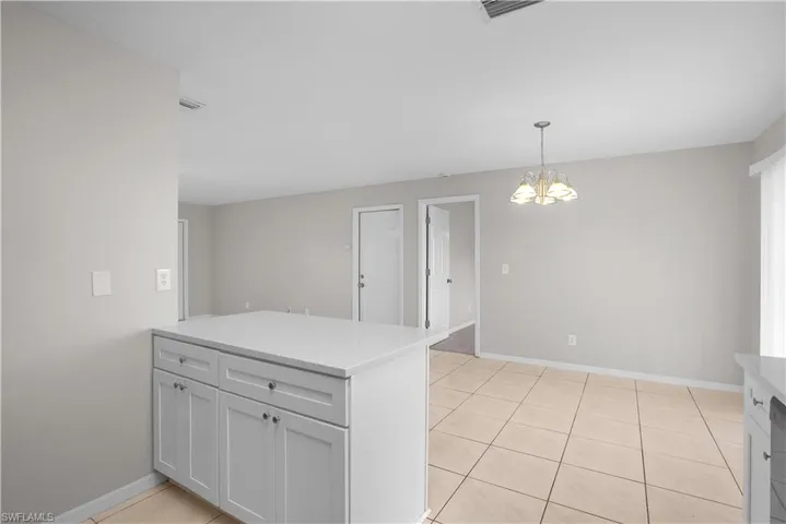 Kitchen island featuring white shaker cabinetry and a light-toned countertop, with a partial view of an adjacent dining area