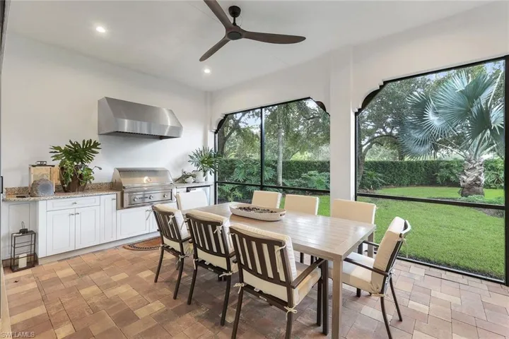 Screened in lanai with outdoor kitchen featuring a natural gas grill, mini fridge and dining table and chairs