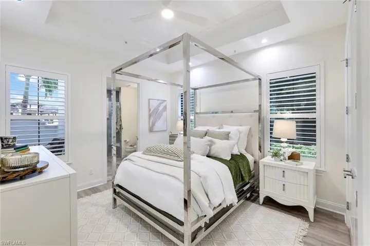 Bedroom featuring light wood-type flooring, a tray ceiling, ceiling fan, and ensuite bathroom
