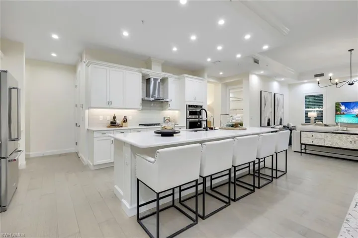 Kitchen with a kitchen island with sink, light hardwood / wood-style floors, white cabinetry, backsplash, and wall chimney range hood